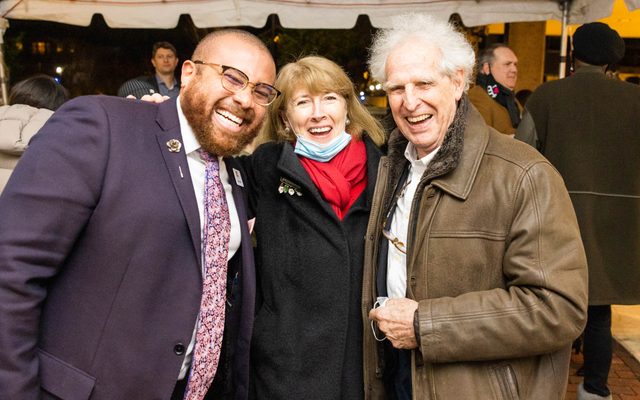 Three supporters in coats coats smiling for the camera.