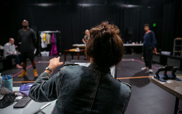 The back of Director Taibi Magar as she works with the actors in rehearsal.