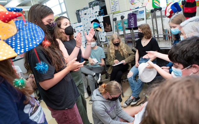 A group of students speak to one another while holding and wearing hats.