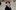 Annaliese Wilbur in a black jacket and large white headphones smiles broadly on a cobblestone street.