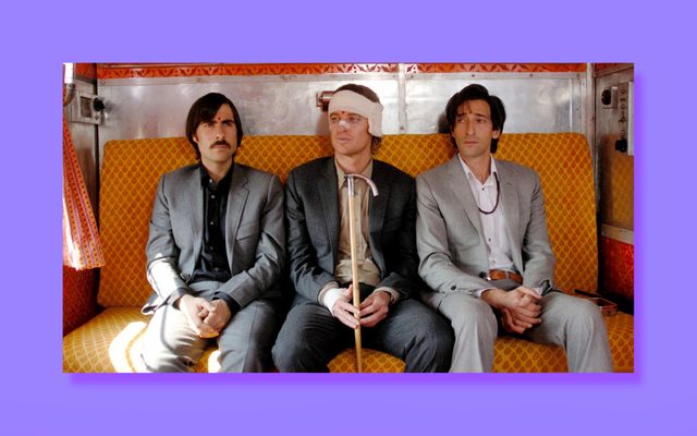 Jason Schwartzman, Owen Wilson, and Adrien Brody sit on an orange bench in a train cabin.